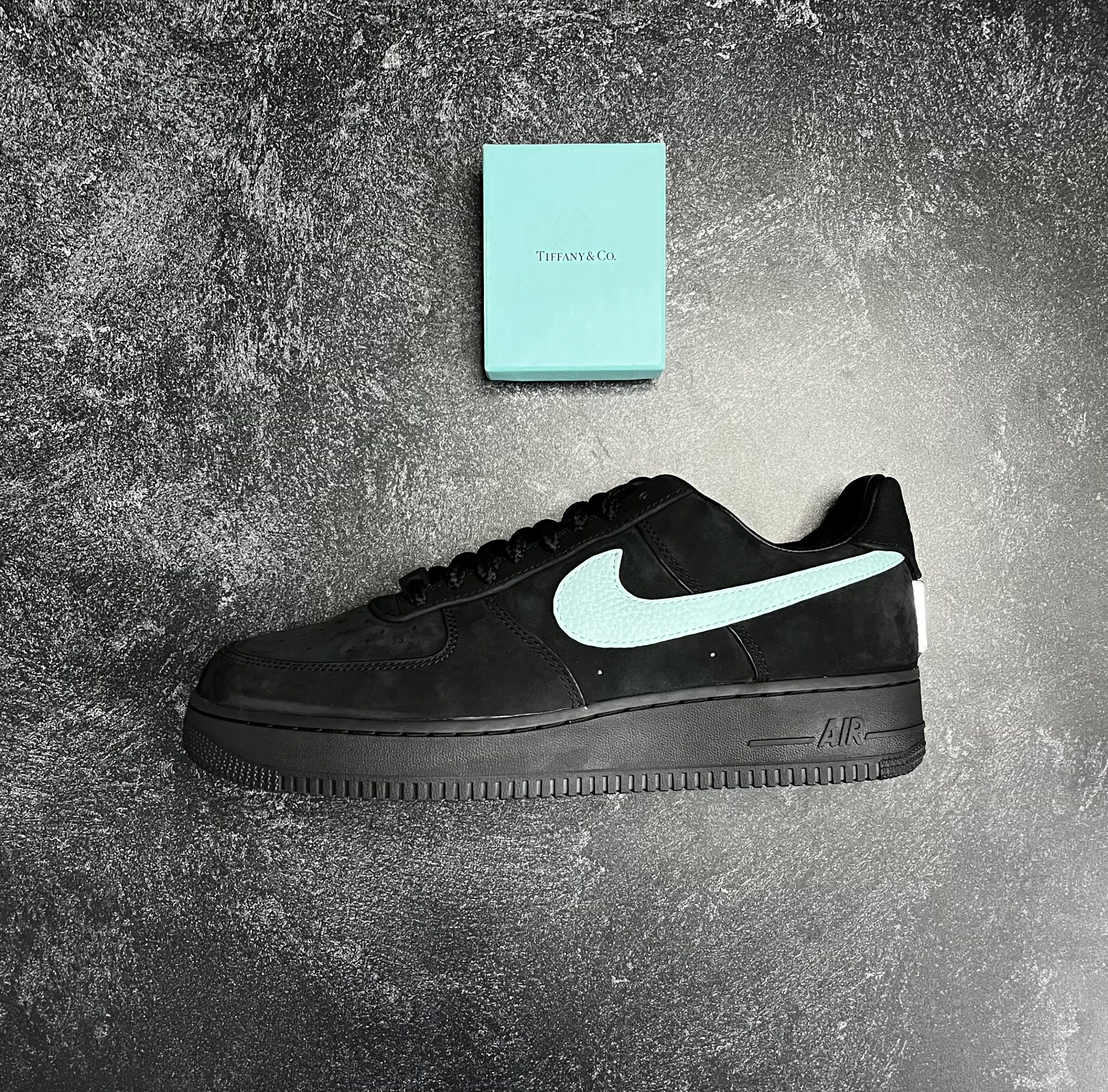 Black Nike Air Force 1 low with white Swoosh side profile on grey textured background